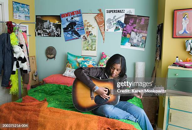 teenage girl (15-17) playing acoustic guitar on bed - girl black hair room stock pictures, royalty-free photos & images