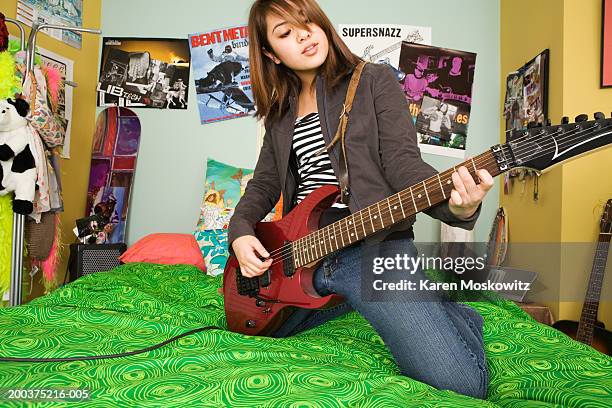 teenage girl (14-16) kneeling on bed, playing electric guitar - woman electric guitar stock pictures, royalty-free photos & images