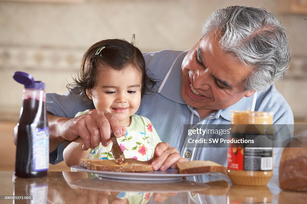 Grandfather helping granddaughter (12-15 months) make sandwich