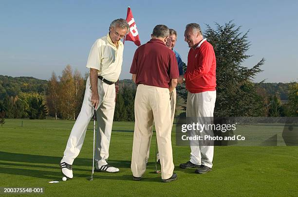 four men on golf green, one pushing ball into hole with foot - golf cheating stock-fotos und bilder