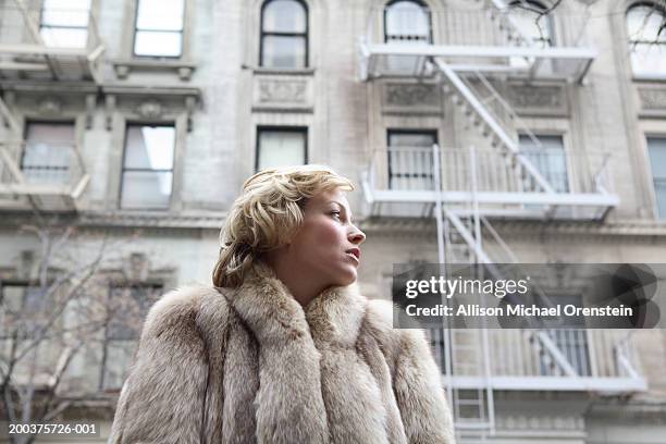 woman in fur coat on street looking to side, low angle view - pelzmantel stock-fotos und bilder