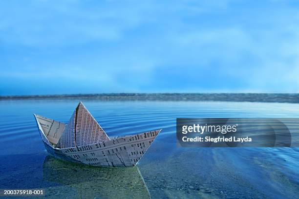 paper boat made from financial newspaper floating in shallow water - toy boat stock pictures, royalty-free photos & images