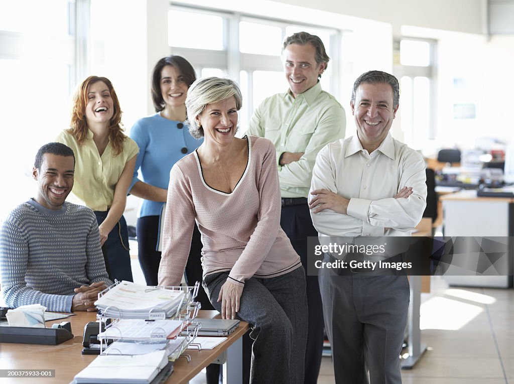 Group of businessmen and women in office, smiling, portrait