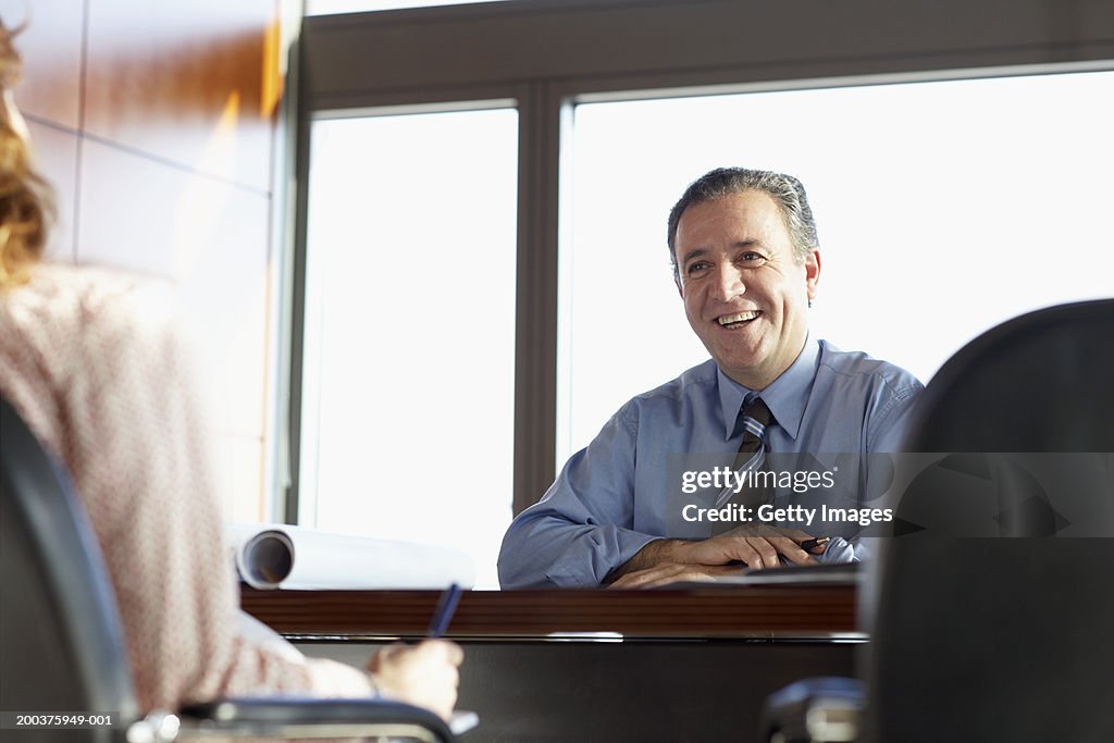 Businessman at desk smiling at businesswoman, low angle view