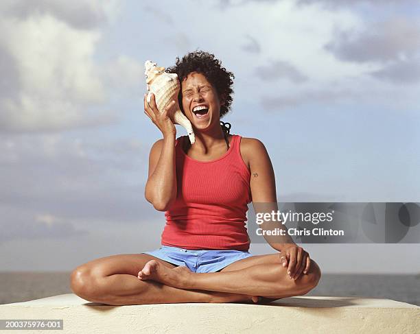 woman holding conch shell to ear, laughing - human ear stockfoto's en -beelden