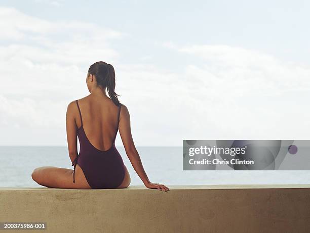 young woman in leotard sitting on ledge, rear view - eendelig zwempak stockfoto's en -beelden