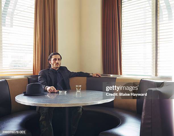 young man sitting at table with drink and cigarette, portrait - gangster foto e immagini stock