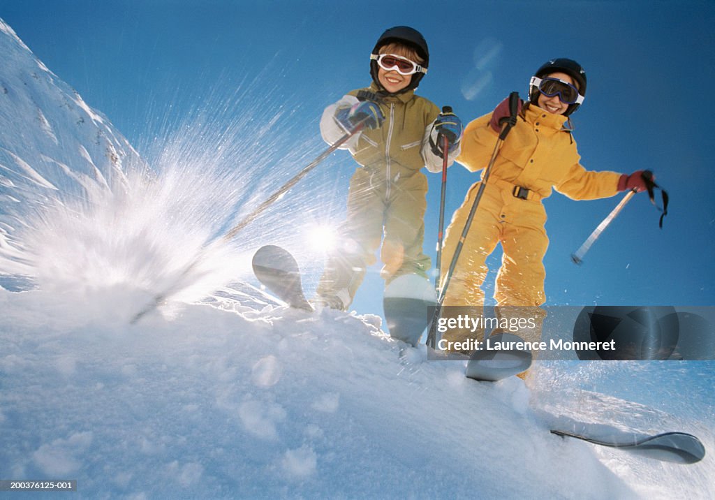 Brother and sister (8-12) on ski slope, smiling, low angle view