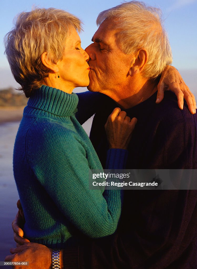 Senior couple on beach, kissing, side view