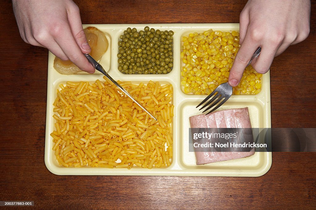 Young man eating food off tray, overhead view, close-up of hands