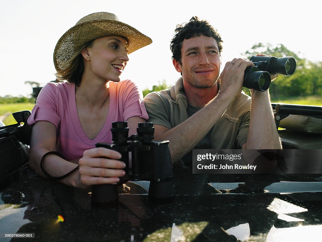 Couple on safari in 4x4 holding binoculars, smiling