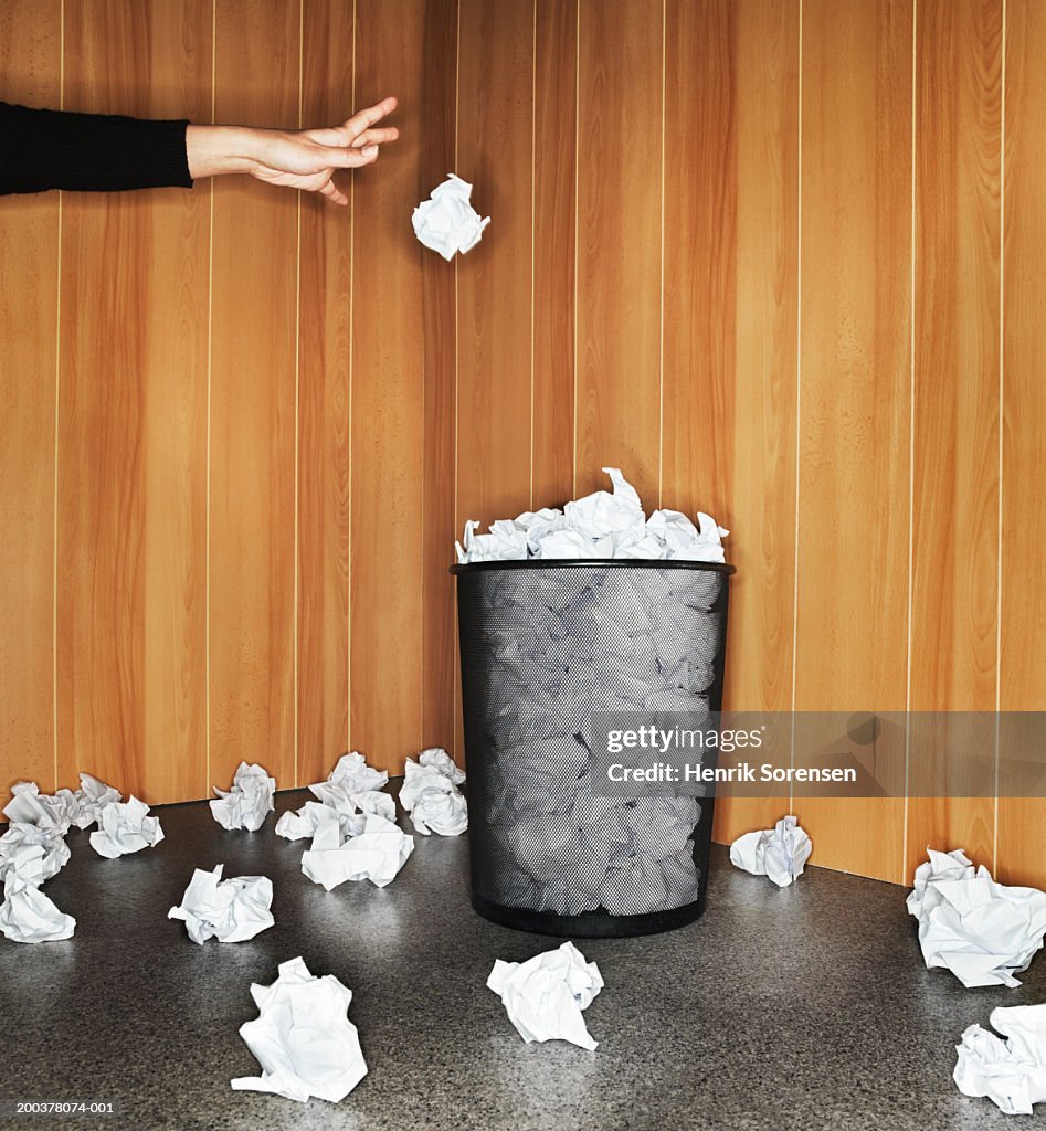 Woman throwing paper in waste paper bin, close-up of hand