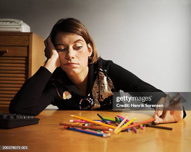 woman at desk playing with coloured pencils, head in hand - perder el tiempo fotografías e imágenes de stock