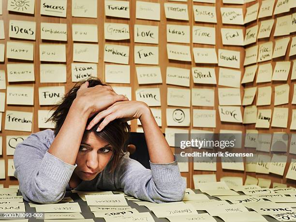 woman at desk surrounded in adhesive notes, head in hands - next single word stock-fotos und bilder