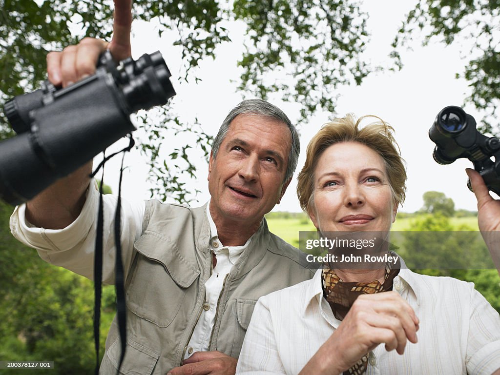 Couple d'âge mûr tenant jumelles, homme souriant pointant vers le haut,