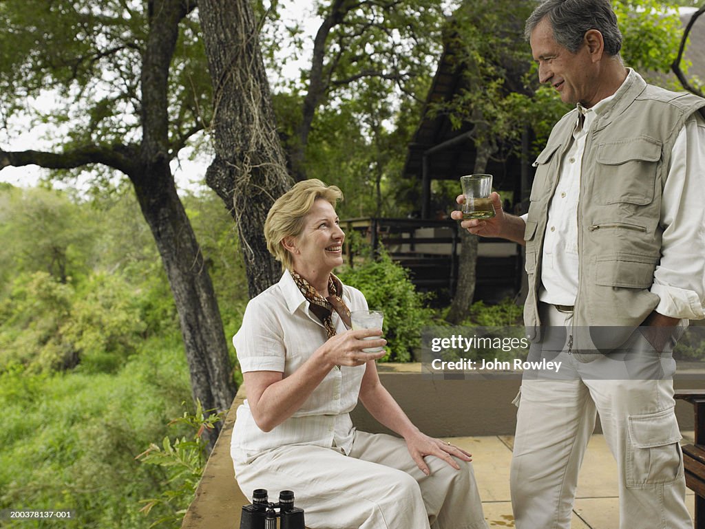 Mature couple having drinks on terrace at lodge, smiling