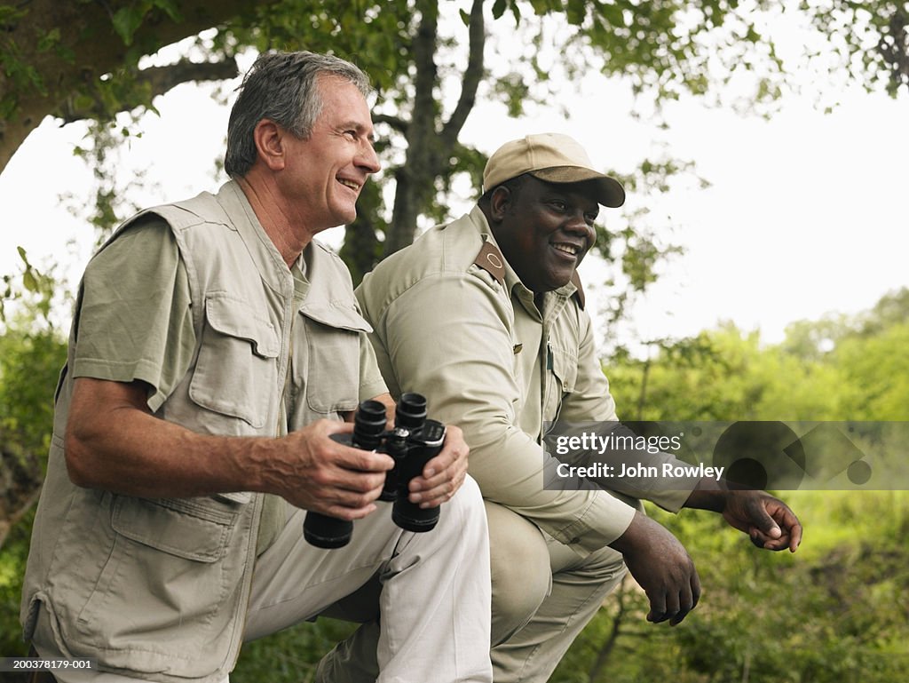 Senior Mann holding Ferngläser auf safari mit Reiseführer, Lächeln