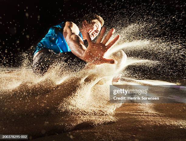 male athlete landing in sand, surface level - verspringen stockfoto's en -beelden
