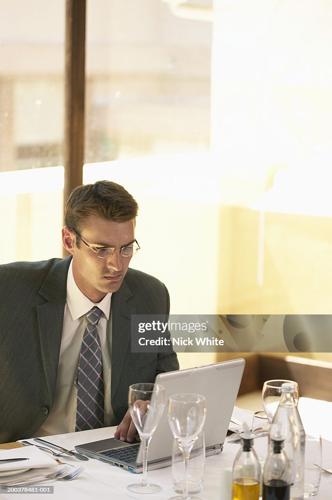 Young businessman using laptop at restaurant table