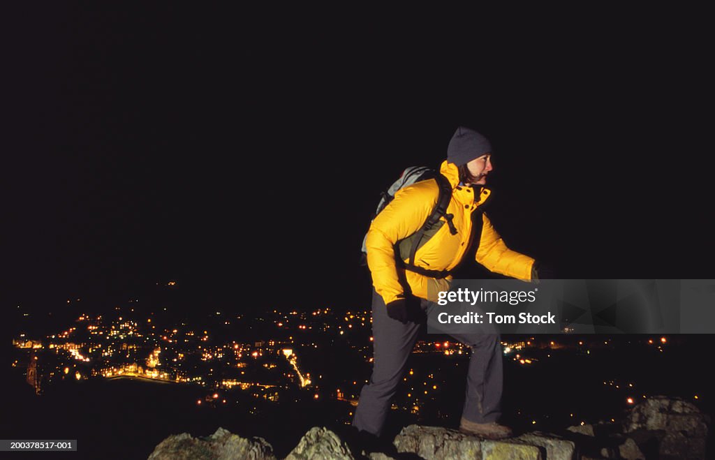 Woman hiking on hill, town lights in background, night