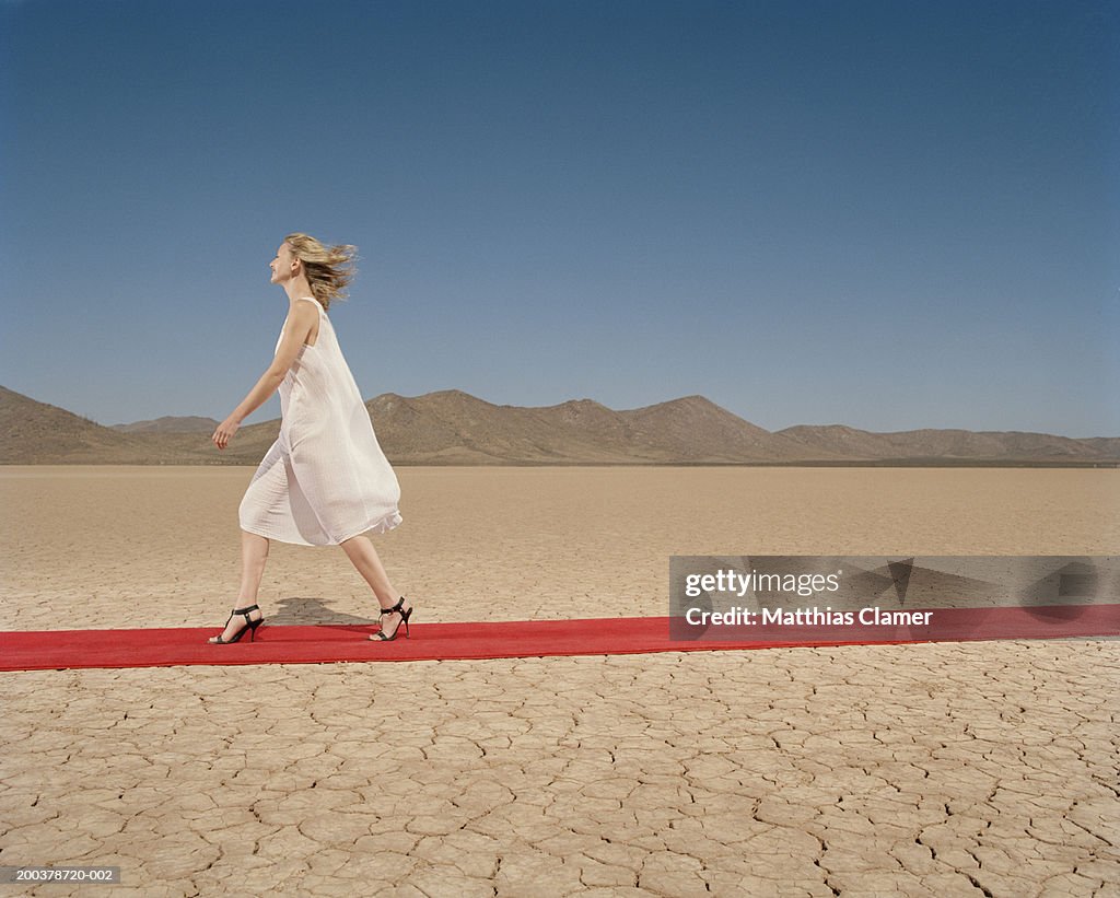 Woman walking down red carpet in desert, smiling, side view