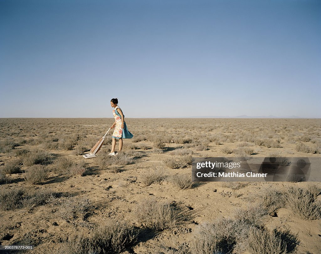 Young woman vacuming in desert, side view