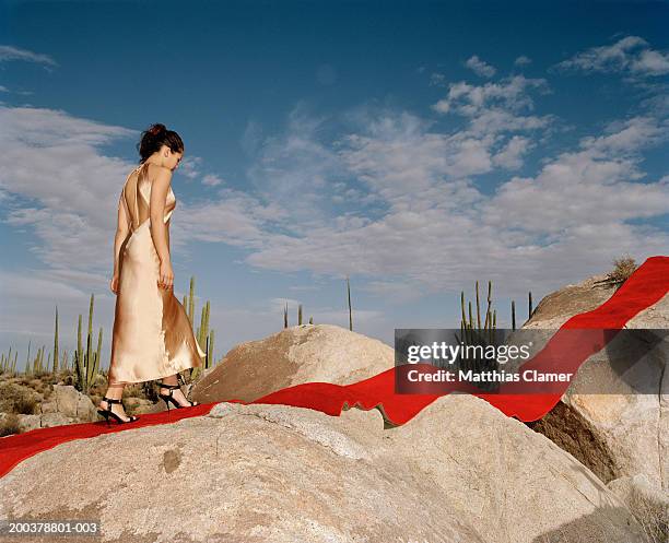 young woman walking on red carpet laid on rocks, side view - abendgarderobe stock-fotos und bilder