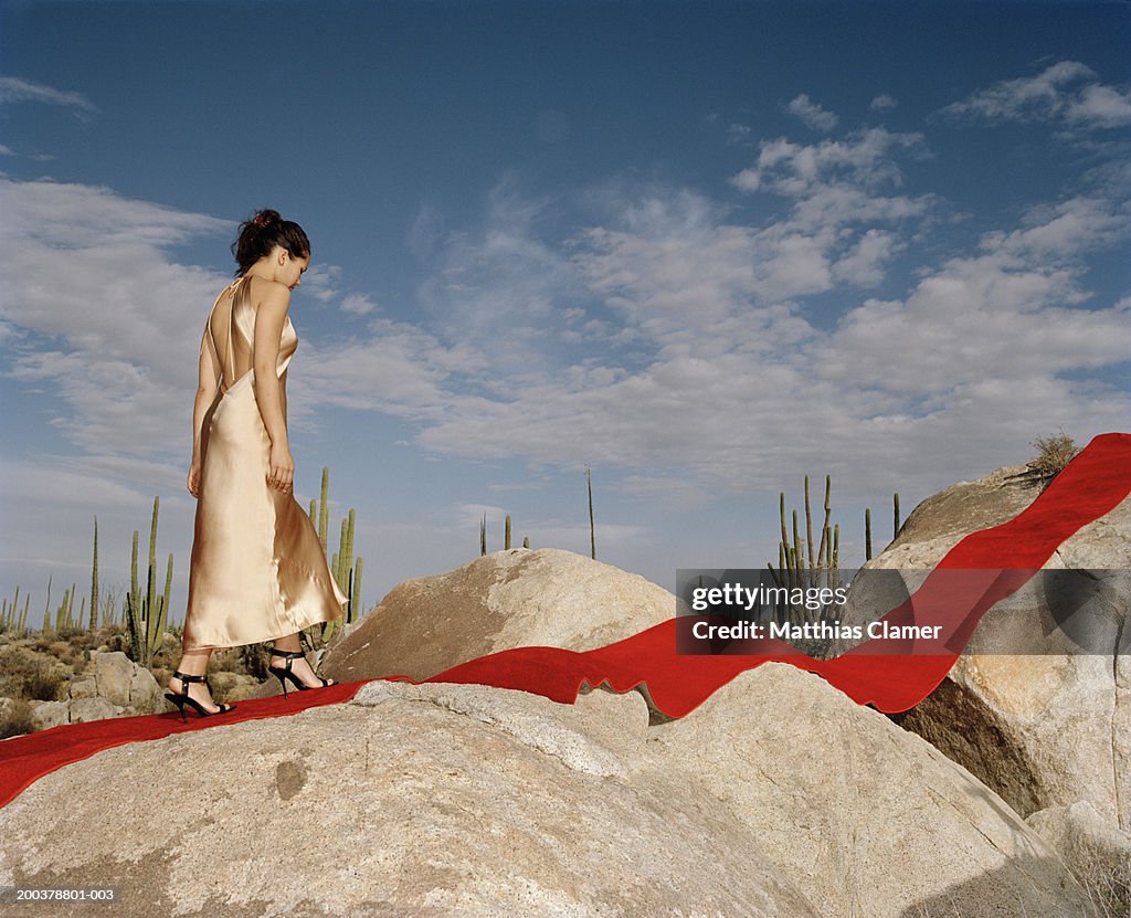 Young woman walking on red carpet laid on rocks, side view