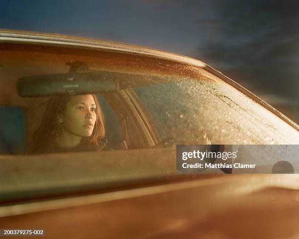 young woman sitting behind wheel of car, side view - regen auto stock-fotos und bilder