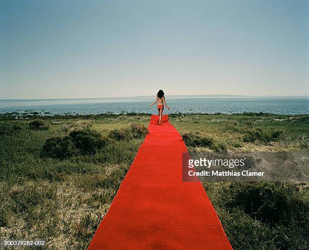 young woman in bikini walking on red carpet near ocean, rear view - red carpet event stock-fotos und bilder