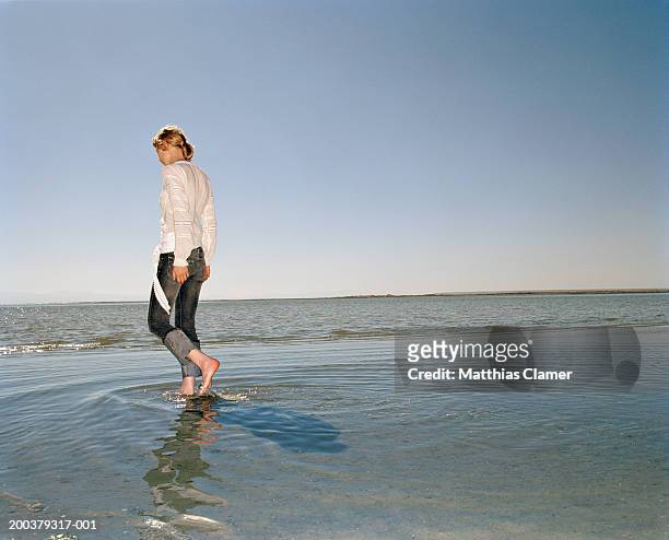 young woman walking in ocean, side view - wet jeans stock-fotos und bilder