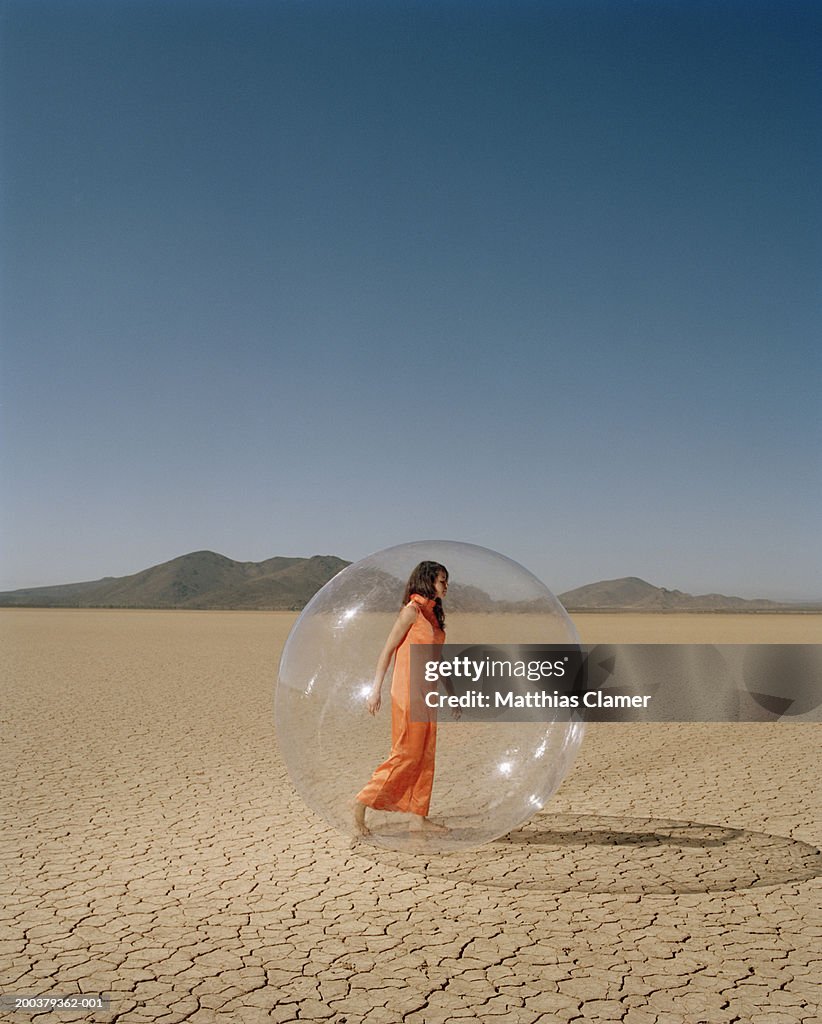 Young woman in desert walking in plastic bubble, side view