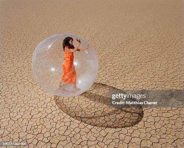 young woman in desert walking in plastic bubble, side view - people inside bubbles stock-fotos und bilder