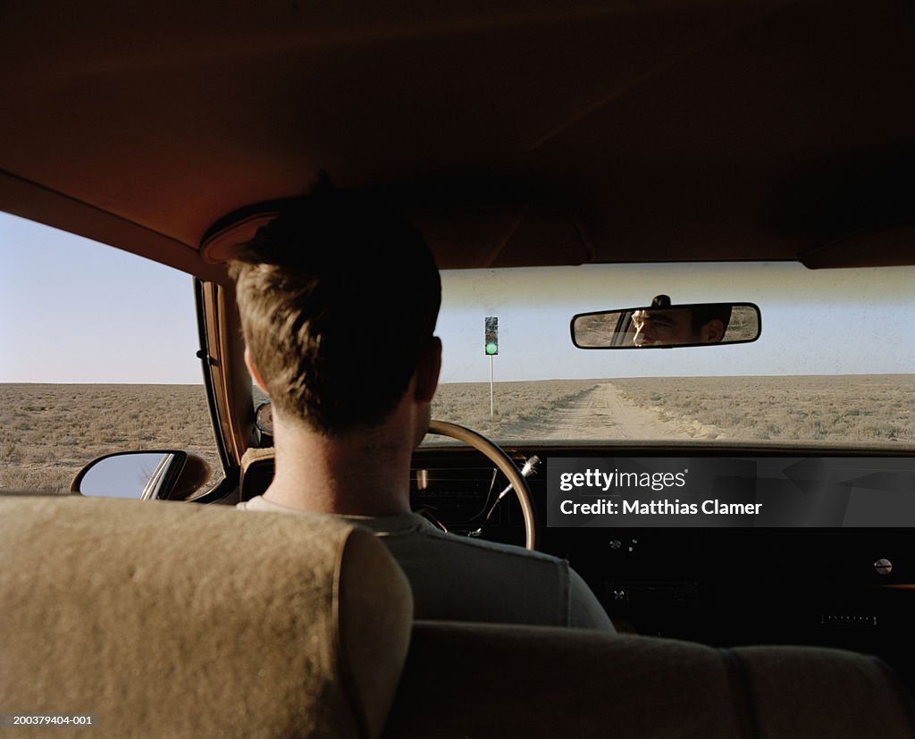 Man driving past traffic light on desert road, rear view, close-up