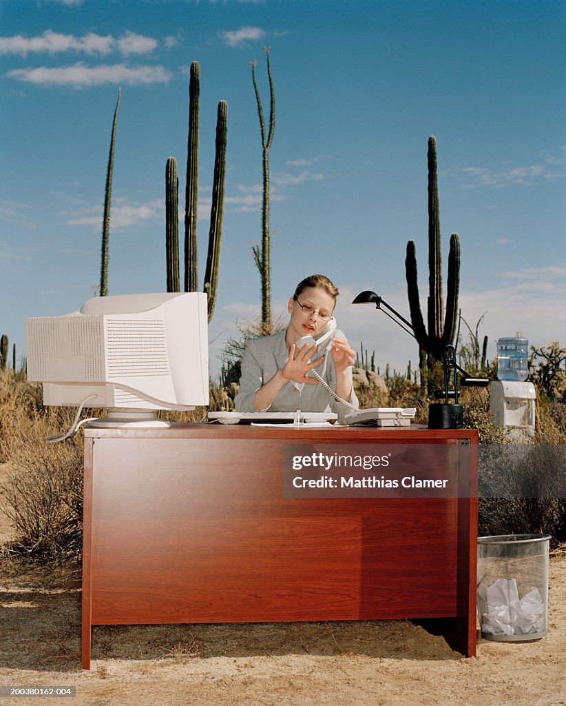 Businesswoman on telephone painting nails at desk in desert