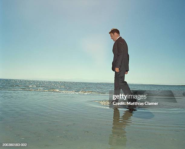 businessman walking through ocean, side view - knöcheltief im wasser stock-fotos und bilder