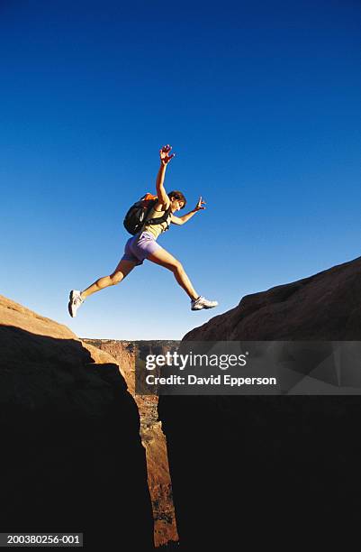 young woman jumping over rock crevice, low angle view - crevice stock pictures, royalty-free photos & images