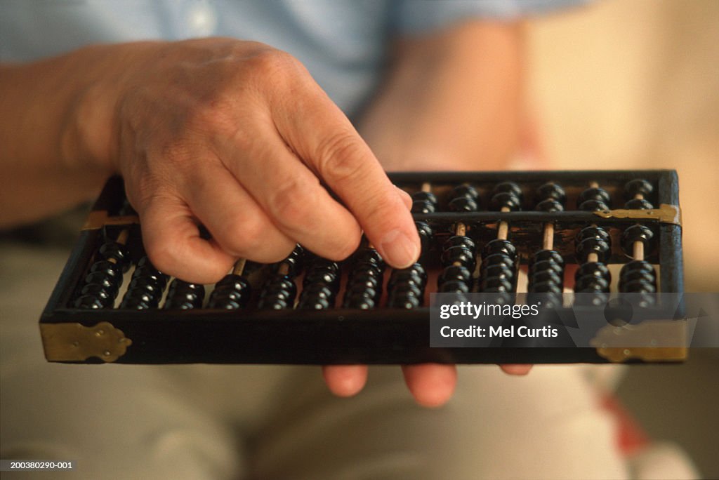 Mature man holding abacus, mid section (focus on hand and abacus)