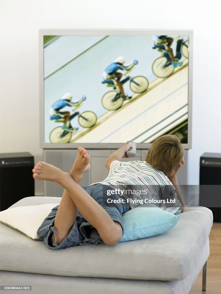Boy (7-9) relaxing in living room watching television, rear view