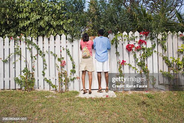 young couple looking over white picket fence, rear view - envy stock pictures, royalty-free photos & images