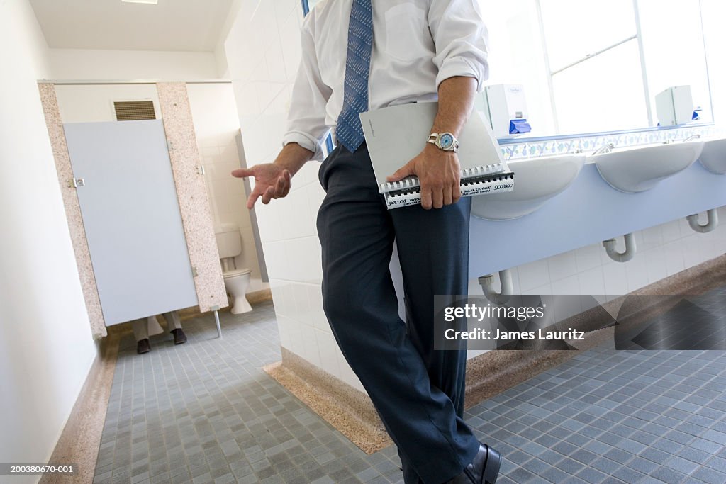 Businessman holding file leaning against sink in office toilets