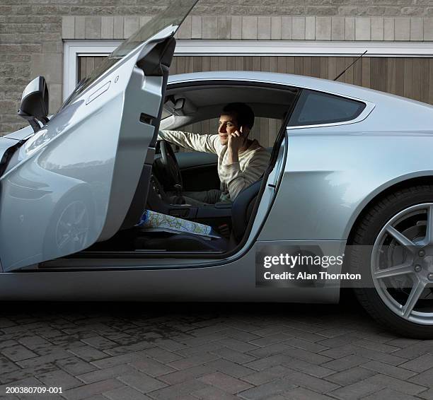 young man sitting in car, using mobile phone, side view - inside car stockfoto's en -beelden