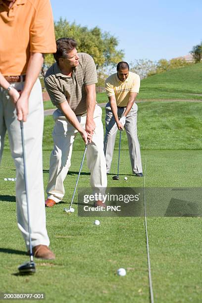 three male golfers hitting golf balls at driving range - driving range stock pictures, royalty-free photos & images