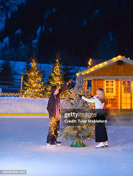 couple putting lights on christmas tree, skating on ice rink - aspen tree stockfoto's en -beelden