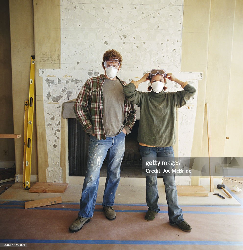 Couple with masks standing in living room under construction