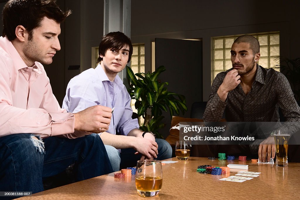 Three young men playing poker, two watching other looking at cards