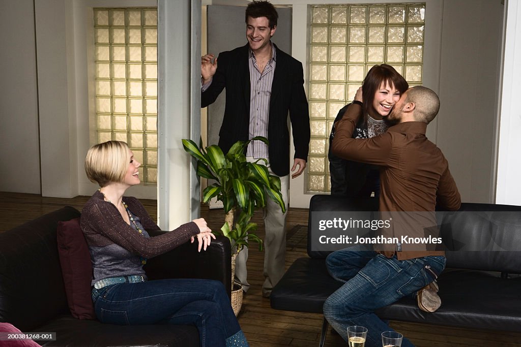 Couple leaving another couple's home, woman kissing man goodbye