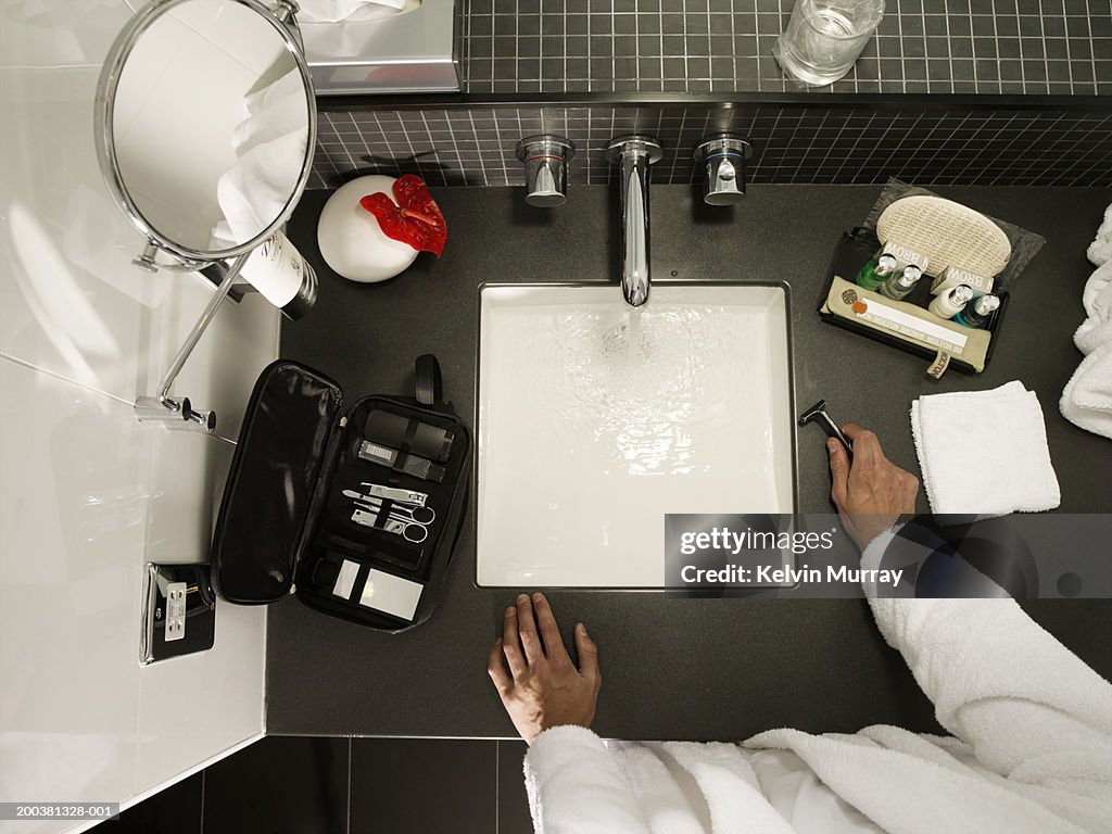 Man standing at bathroom sink, filling basin with water, overhead view