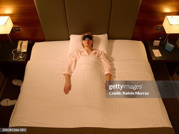 woman sleeping in middle of double bed, wearing sleeping mask - king size bed stockfoto's en -beelden