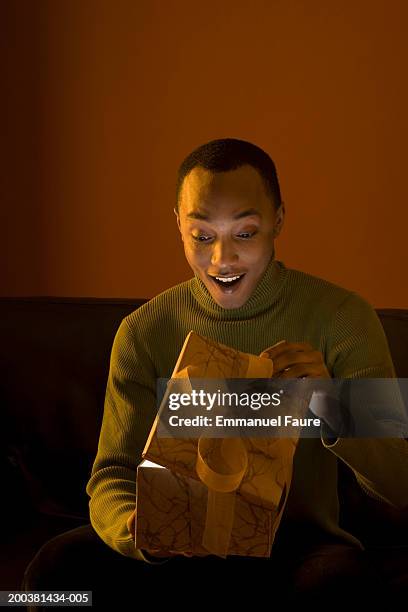young man looking at open gift box, mouth open, smiling - surprise gift foto e immagini stock